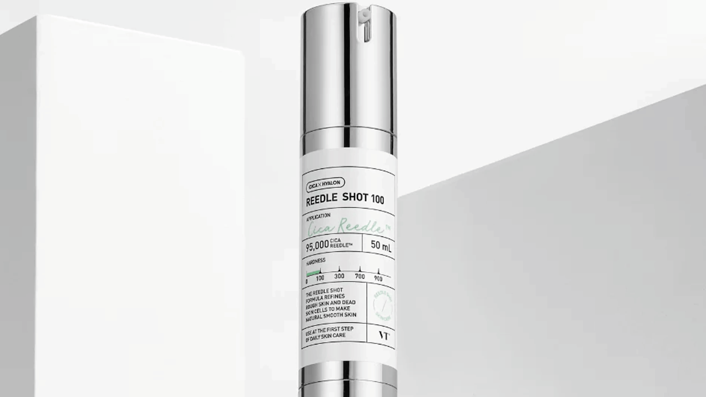 VT Cosmetics ReeDle Shot 100, en hyaluronsyra-serum med Cica, presenteras i en elegant silver- och vit flaska. Den är designad för att förfina grov hud och döda hudceller för en naturligt mjuk hud. Flaskan står mot en minimal vit bakgrund.